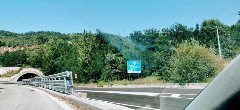 Autostrade e segnaletica orizzontale: 10 regole per una guida sicura 4 Auto strada in zona collinare con tunnel e segnale informativo, paesaggio naturale e traffico leggero, vista dinamica di un percorso stradale in Italia.
