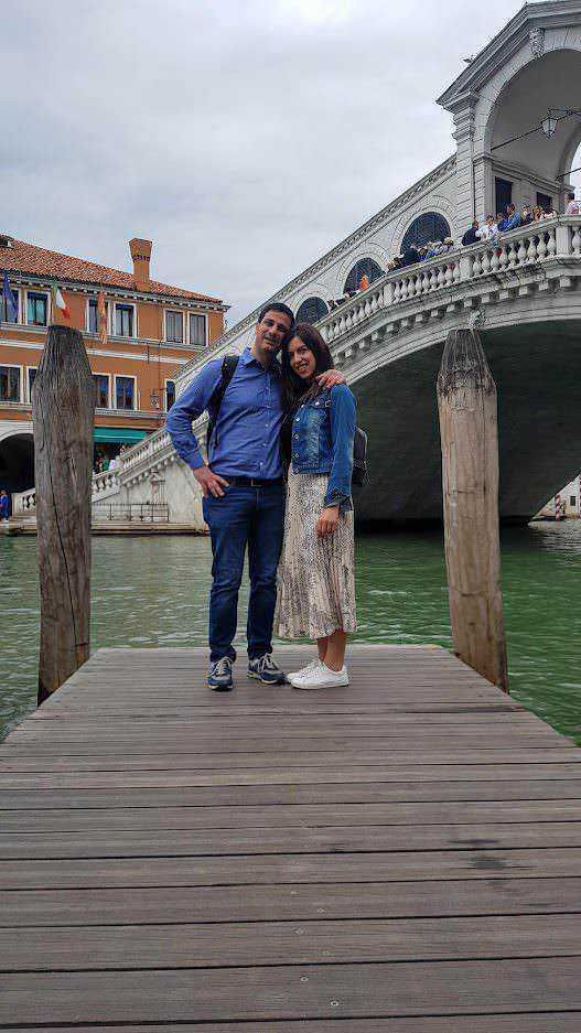 Vignetta di una coppia felice che si abbraccia sul molo a Venezia con il Ponte di Rialto sullo sfondo, atmosfera romantica e scenografica.