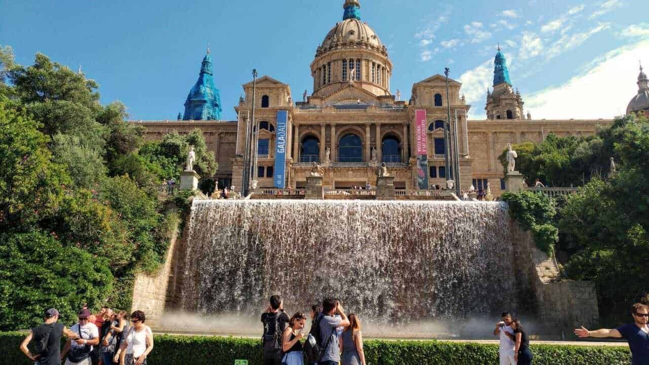 Palazzi storici e fontana a Montjuïc, Barcellona, con turisti che visitano il luogo e cielo sereno.