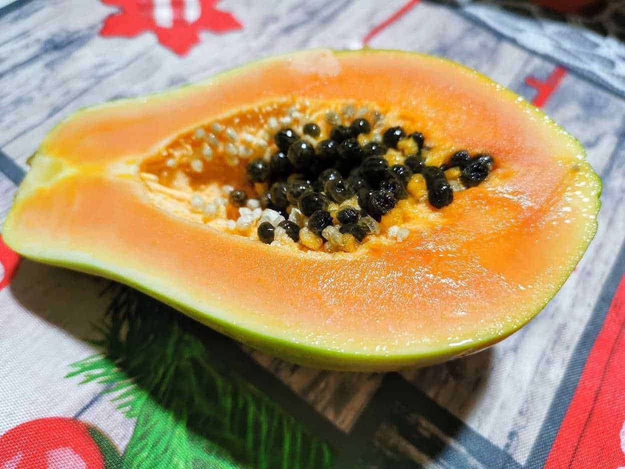Papaya fresca e succosa con semi neri e bianchi, vista dettagliata di metà frutto collocato su un tavolo in stile rustico con tovaglia colorata, alimenti tropicali sani e deliziosi.