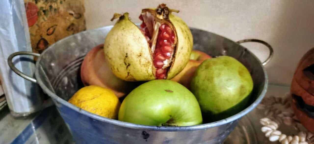 Pere non mature e melograno in una ciotola di metallo, frutta fresca e naturale su tavolo.