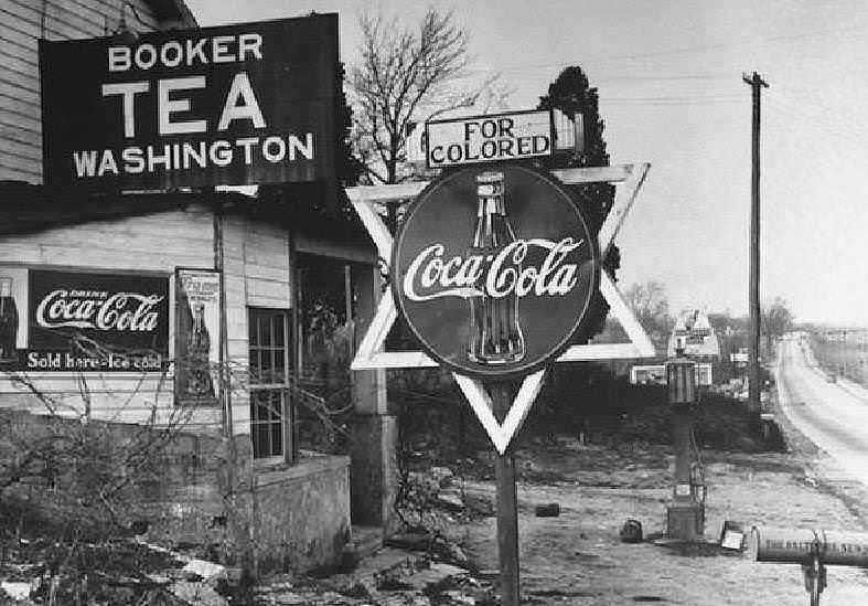 Bottiglia di Coca-Cola vintage e insegne pubblicitarie in una strada storica americana senza colore.