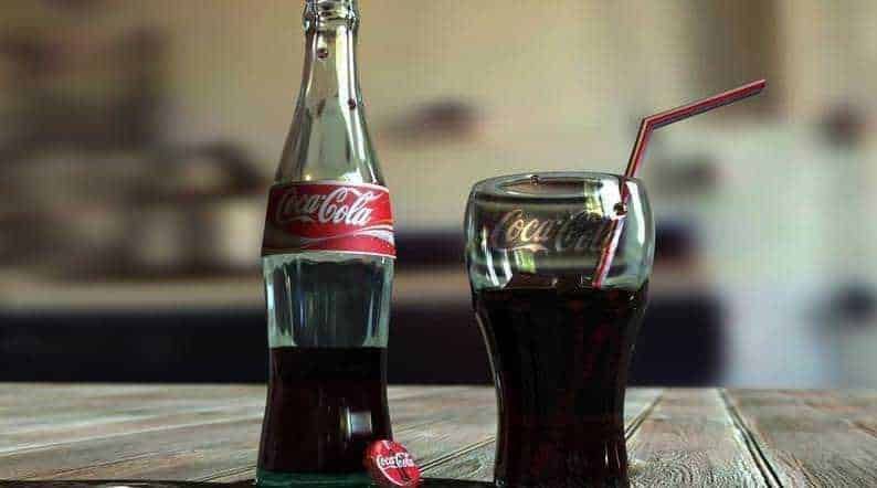 Bottiglia e bicchiere di Coca-Cola su tavolo in legno, bevanda analcolica rinfrescante e popolare.