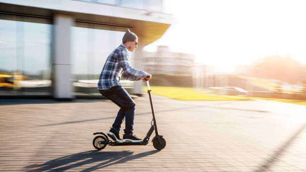 L'immagine mostra un giovane che si diverte a pattinare su uno scooter elettrico all'aperto, in un'area urbana moderna al tramonto, evidenziando libertà, mobilità e stile di vita attivo.
