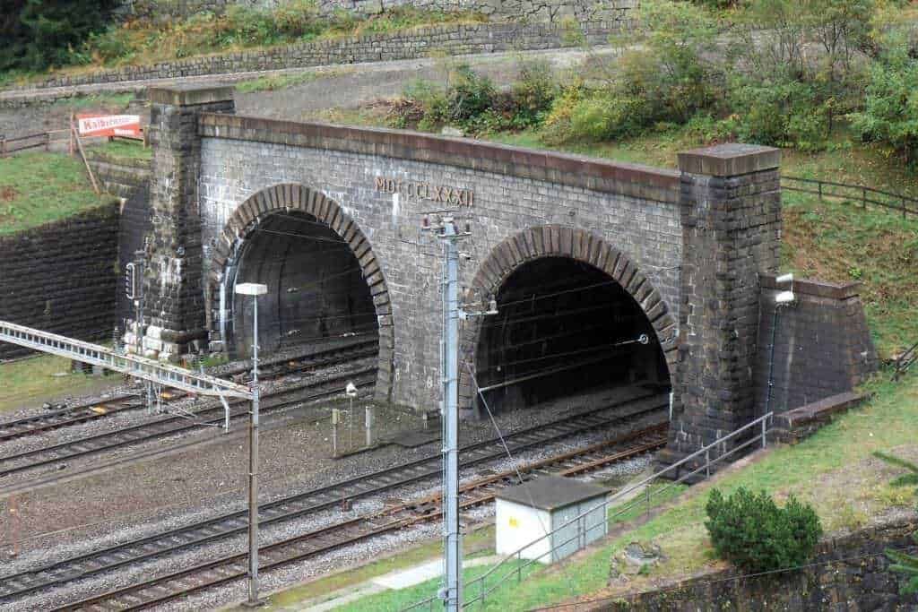 Vecchio sottopassaggio ferroviario in pietra con arcate, situato in un'area collinare verde, parte di un’antica rete ferroviaria in Italia, rappresenta un esempio di architettura storica delle ferrovie.