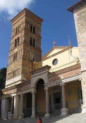 Campanile storico di un'antica chiesa in Italia con dettagli architettonici in mattoni e pietra sotto un cielo azzurro.