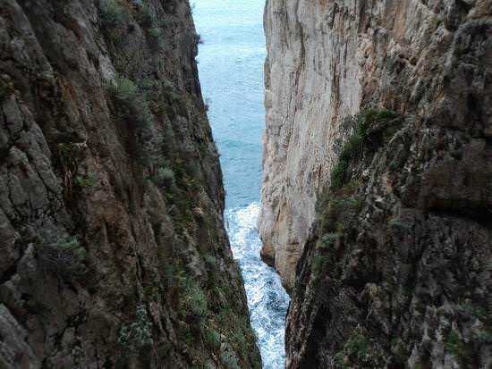 Scogliera calcarea con stretto tra le rocce che si apre sul mare, paesaggio naturale mozzafiato in Italia.