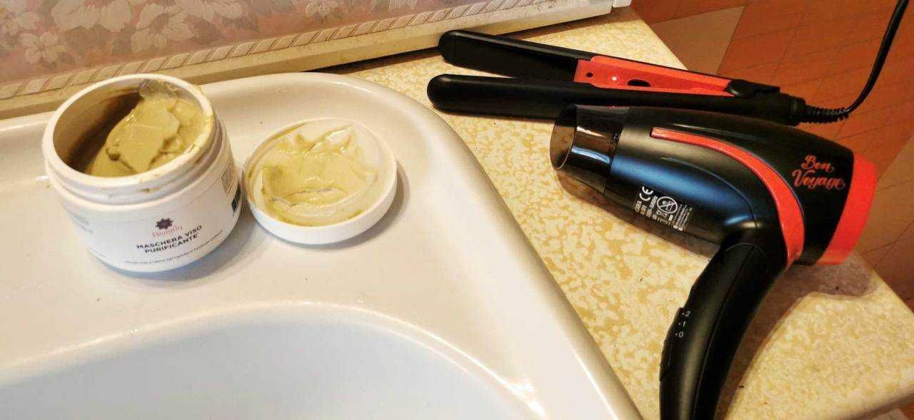 Maschera viso e piastra per capelli su tavolo, cura della bellezza e stile, prodotti per capelli e trattamento viso, ambientazione quotidiana di bellezza e benessere, sulla superficie di un tavolo in casa.