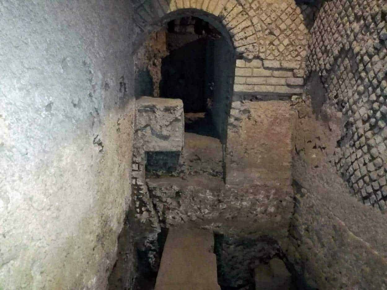 Motivo di una vecchia struttura in mattoni e pietra, probabilmente parte di un sito storico o archeologico con un arco e passaggi sotterranei, evidenziando l'architettura antica e il restauro conservativo.