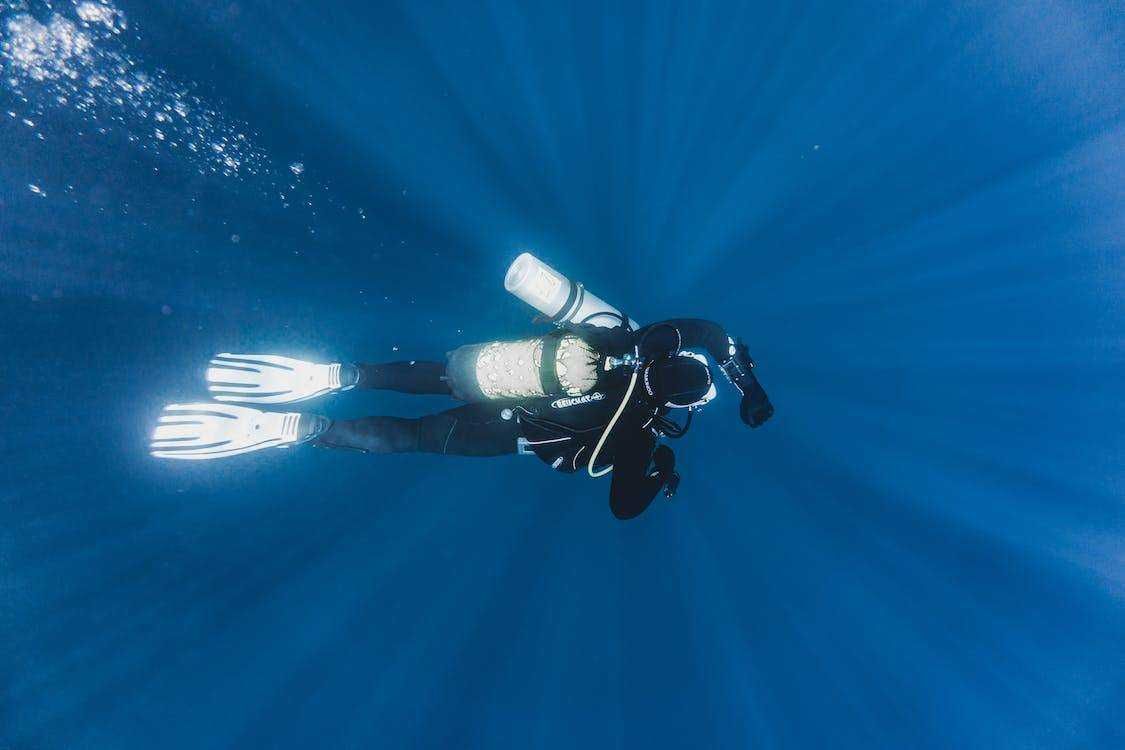 Immersione subacquea in acqua blu con attrezzatura da diving, snorkel, muta e bombole, esplorando il mondo marino e la fauna sottomarina. Attività di avventura e turismo subacqueo.
