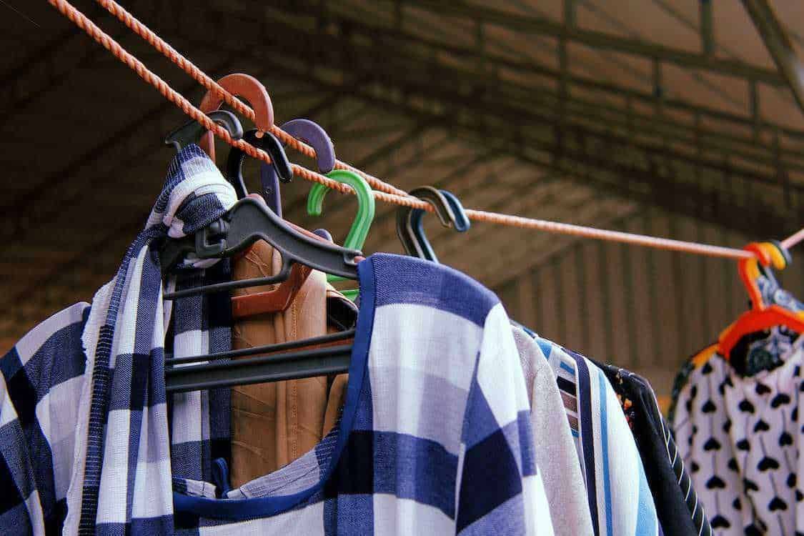 Vestiti estivi stesi ad asciugare su un filo all'aperto, con vari capi come magliette, pantaloni e abiti, in un ambiente domestico soleggiato, ideali per il blog di moda e lifestyle.
