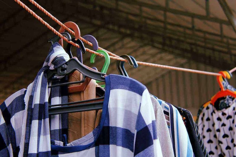 Lavanderia 5 tipologie di lavaggio a secco 2 Vestiti estivi stesi ad asciugare su un filo all'aperto, con vari capi come magliette, pantaloni e abiti, in un ambiente domestico soleggiato, ideali per il blog di moda e lifestyle.