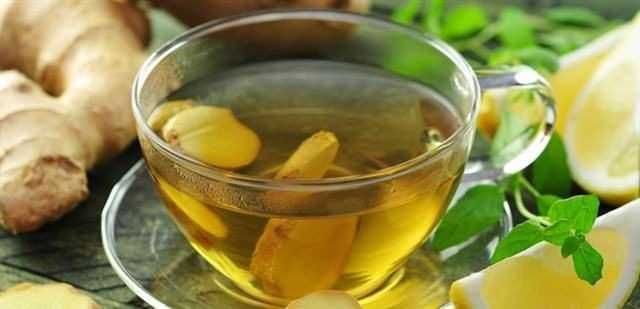 Tazza di tè allo zenzero con fette di limone e foglie di menta, ideale per riscaldarsi e rilassarsi, perfetta per infusioni e benessere naturale.