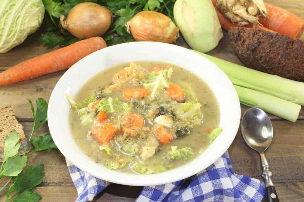 Verdura fresca e ingrediente per minestre fatte in casa, immagine di zuppa di verdure con carote, cipolle, sedano e cavolo in ciotola bianca.