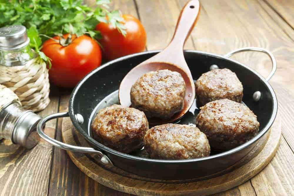 Polpette di carne fatte in casa in padella, preparate con ingredienti freschi, servite con pomodori e aromi, perfette per un pranzo ricco di sapore e qualità alimentare.