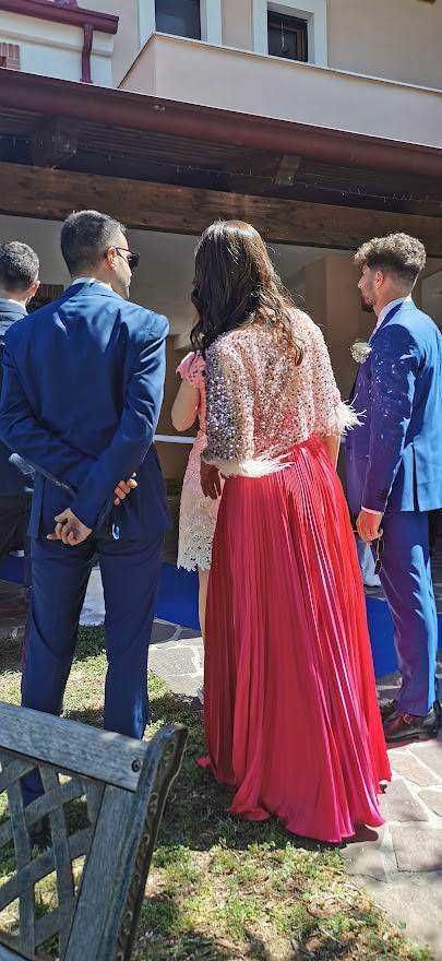 Gli invitati al matrimonio indossano abiti eleganti con uomini in completi blu e donna in abito rosso lungo, ambientazione esterna durante una cerimonia di nozze in Italia.
