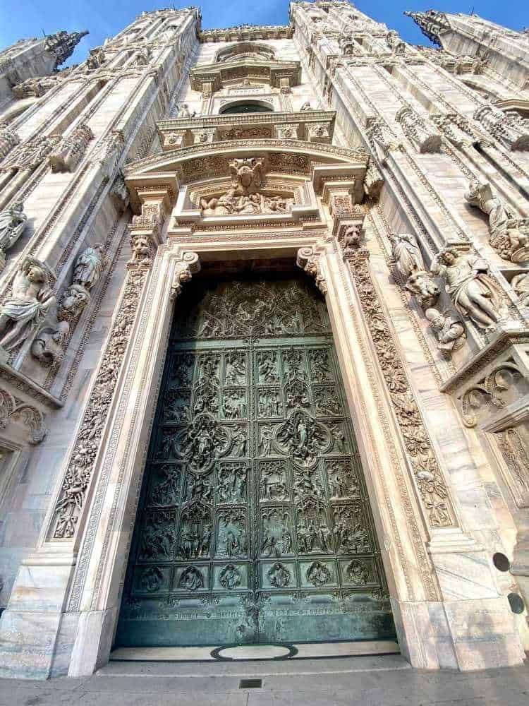 Portale gotico in stile barocco con dettagli scolpiti e statue, ingresso monumentale alla Cattedrale di Milano, ricco di decorazioni artistiche e simboliche, esempio di architettura religiosa italiana.