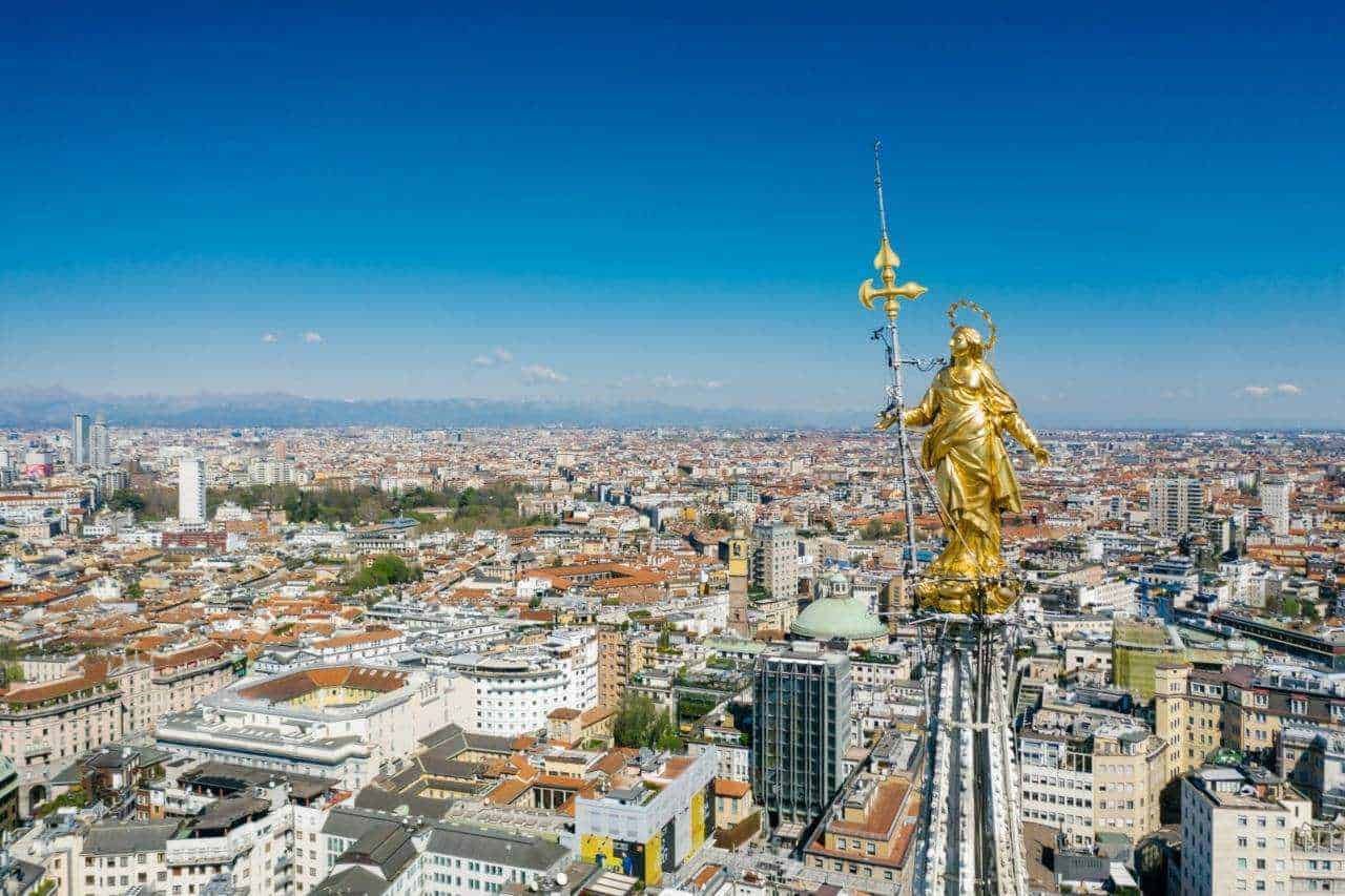 Vetrata con statua di oro di santa Maria sulla cattedrale di Milano, vista panoramica sulla città, skyline di Milano con le Alpi sullo sfondo.