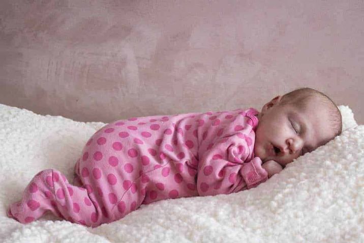 L'importanza del Paracolpi nel Lettino 3 Neonato che dorme su coperta morbida, vestito rosa con pois, riposo sereno, aspetto tranquillo, immagine dolce di un bebè, cura neonatale, infanzia felice, tenerezza, sonno riposante, delicatezza del bambino.