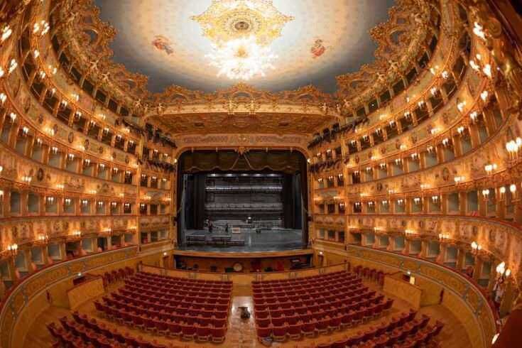 Teatro d'opera storico con arredi dorati e illumintazione calda, palco centrale e sedili eleganti, perfetto per spettacoli culturali e eventi artistici.