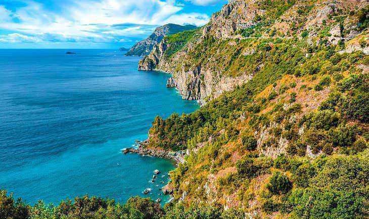 Valle colorato e roccioso che si affaccia sul mare cristallino e turchese della costa italiana, con scogliere alte e vegetazione lussureggiante.