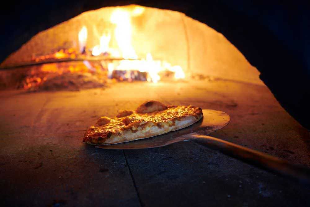 Forno a legna con pizza calda appena sfornata, ambiente tradizionale per autentica pizza napoletana.