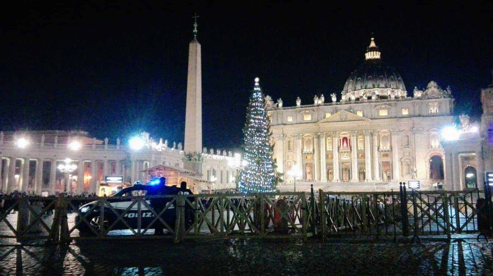 Palazzo di San Pietro in Vaticano illuminato di notte con albero di Natale decorato e polizia in servizio, suggestiva scena natalizia a Roma.
