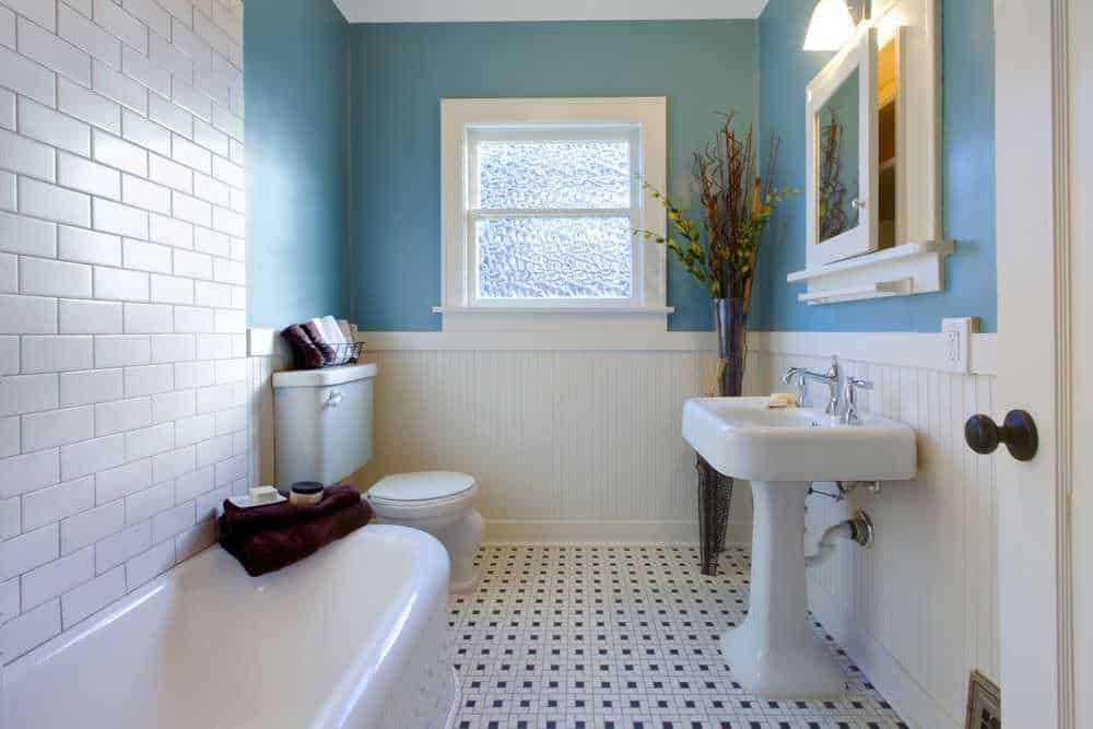 Bagno con pareti azzurre e dettagli bianchi, lavabo e finestra per un ambiente luminoso e accogliente. Arredo semplice e decorazioni floreali creano un'atmosfera rilassante e pulita.