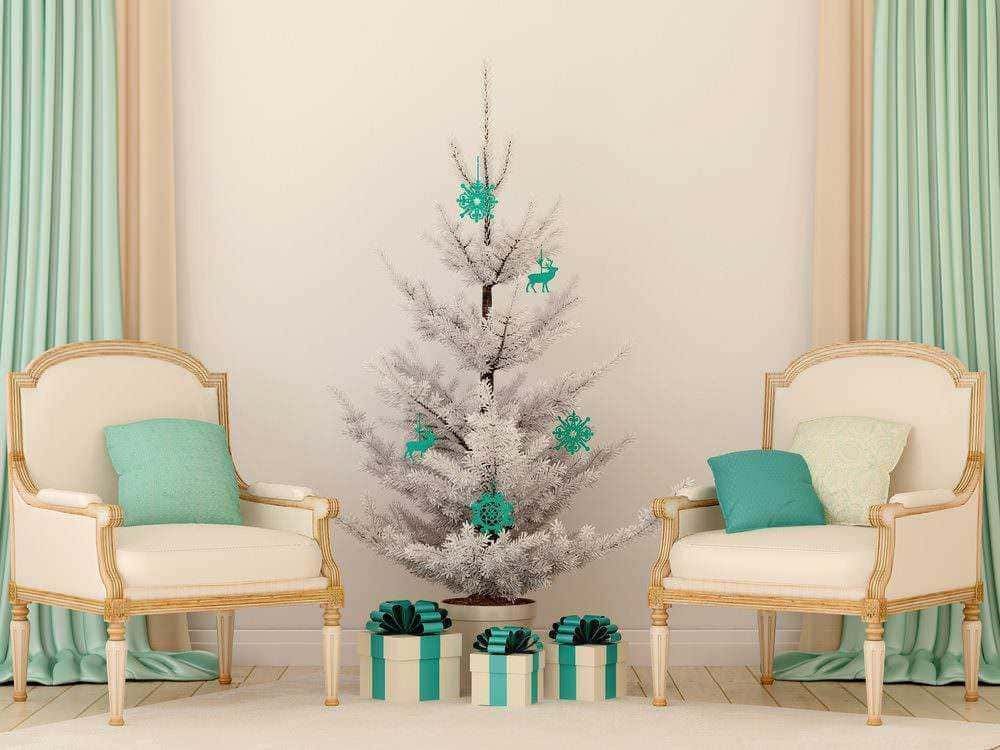 Albero di Natale artificiale bianco decorato con palline e fiocchi di neve blu, eleganti sedie con cuscini in zona soggiorno, atmosfera natalizia raffinata, decorazioni di festa con regali sotto l'albero.