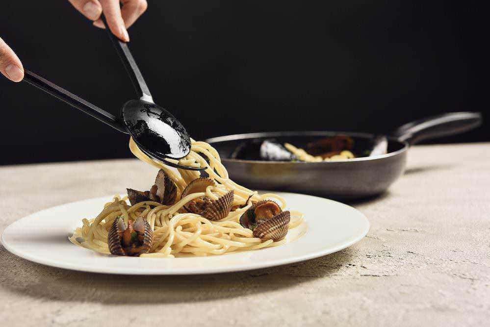 Spaghetti alle vongole in pentola e serviti in piatto bianco, cucina italiana, piatto di pasta con frutti di mare, preparazione di ricette di mare, immagini di cucina tradizionale italiana.