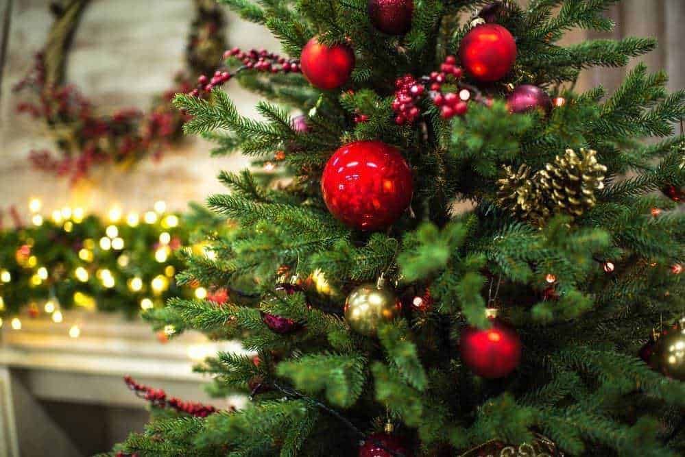 Addobbi natalizi allestiti su un albero di Natale con palline rosse, oro e pigne, illuminazioni che creano un'atmosfera festosa e calda per le festività natalizie.