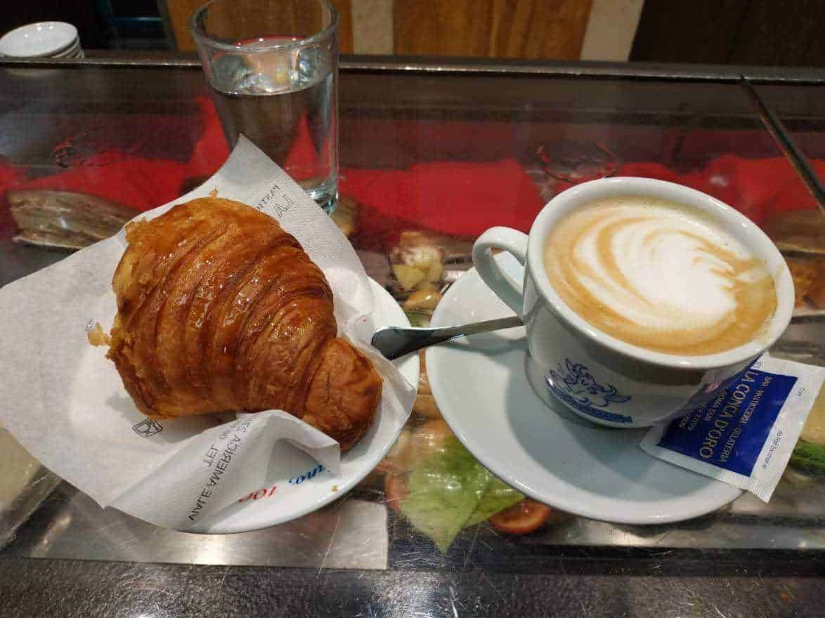 Croissant dorato con cappuccino cremoso serviti in una caffetteria italiana.