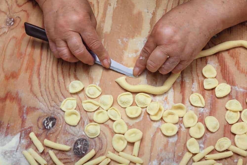Ricette di pasta fatta in casa, preparazione di tortellini con impasto fresco e taglio manuale. Fet|Tortellini fatti a mano, preparazione tradizionale di pasta fresca italiana. Pasta artigianale su superficie di legno rustico.