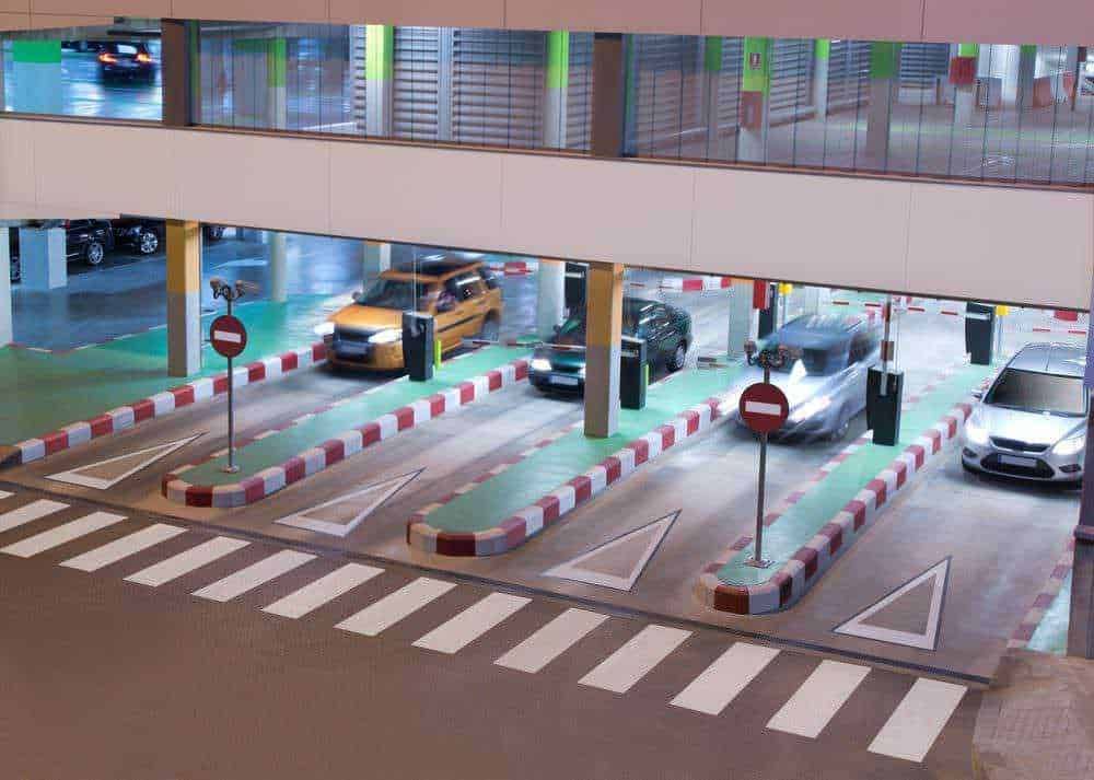 Parcheggio di auto in un centro commerciale, area di ingresso con barriere e segnali di divieto, spazio per veicoli con corsie delimitate e supporti per il pagamento, ambiente moderno e organizzato.