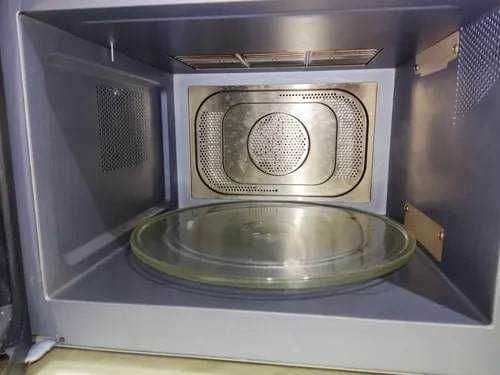 Microonde con piatto girevole e interno in acciaio inox, ideale per riscaldare e cucinare alimenti facilmente, collegato a una ciotola di vetro, mostrato in un ambiente domestico.