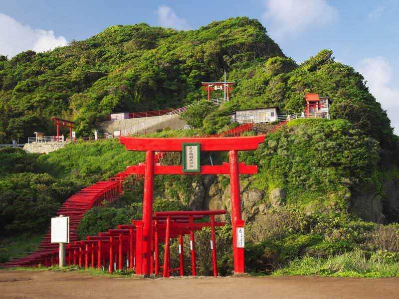 Santuario di Motonosumi 2 Torii rossi e sentiero che conduce a un santuario shintoista tra le colline verdi in Giappone, rappresentazione di spiritualità e cultura giapponese.