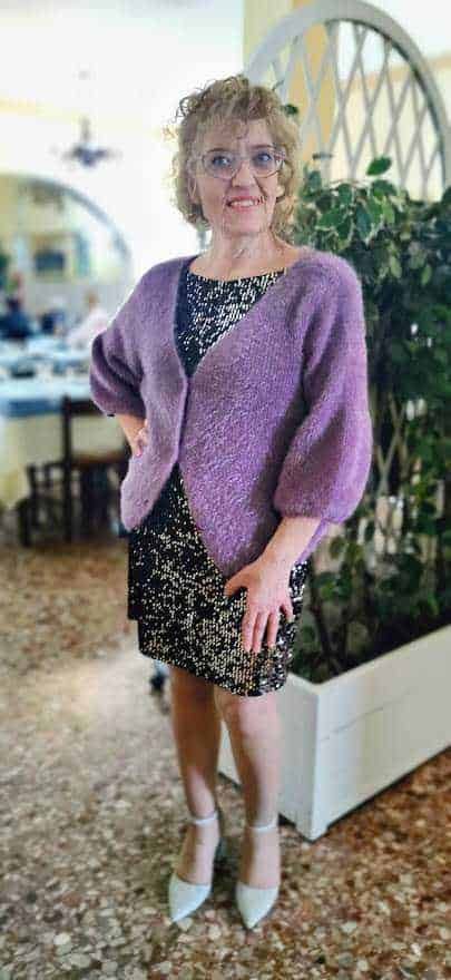 Elegante donna in abito con cardigan viola in ambientazione raffinata e moderna. Perfetta per look casual chic o occasioni speciali, valorizzando stile e personalità.