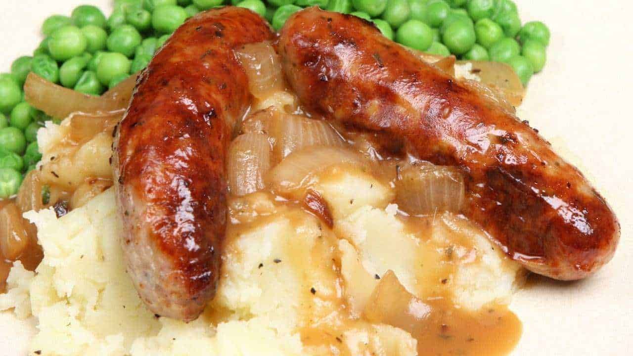 Salsiccia alla griglia con purè di patate e piselli freschi, piatto tradizionale italiano, ricco di sapori autentici.
