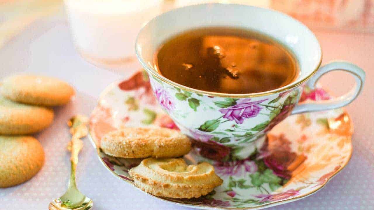 Tazza di tè in una tazza di porcellana decorata con motivi floreali, accompagnata da biscotti tradizionali su un piattino abbinato, ideale per un momento di relax e dolcezza.