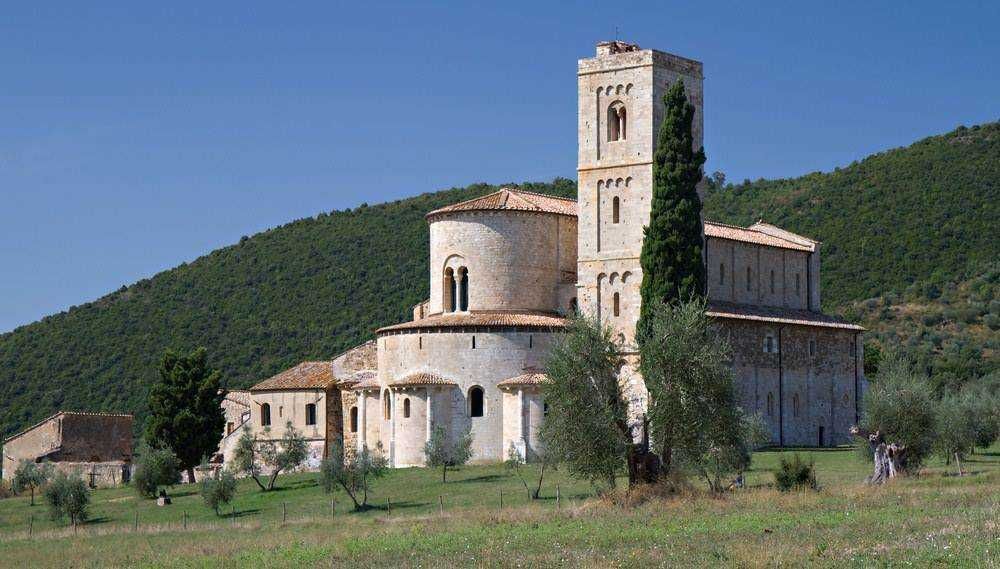 Vecchia chiesa in pietra con campanile e paesaggio verde e collinare sullo sfondo, immersa nella natura, esempio di architettura storica e spirituale.