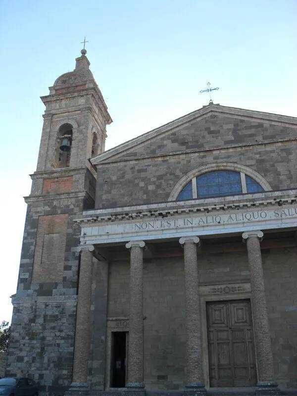 Campanile e facciata di una chiesa storica in pietra, con colonne e un arco, sotto un cielo azzurro. Architettura religiosa italiana, facciata maestosa e dettagli architettonici classici.