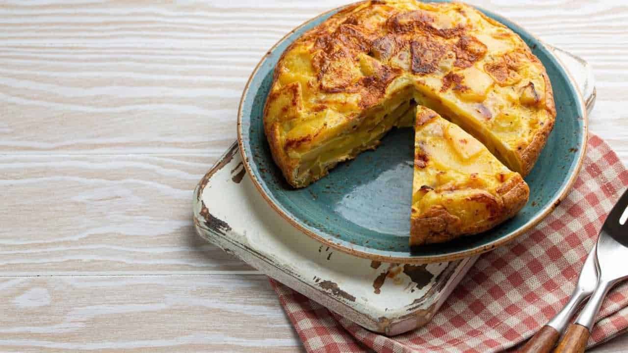 Frittata di patate e formaggio cotta in teglia, pronto da servire, visibile su un piatto azzurro su superficie in legno chiaro, perfetta per ricette di cucina italiana.