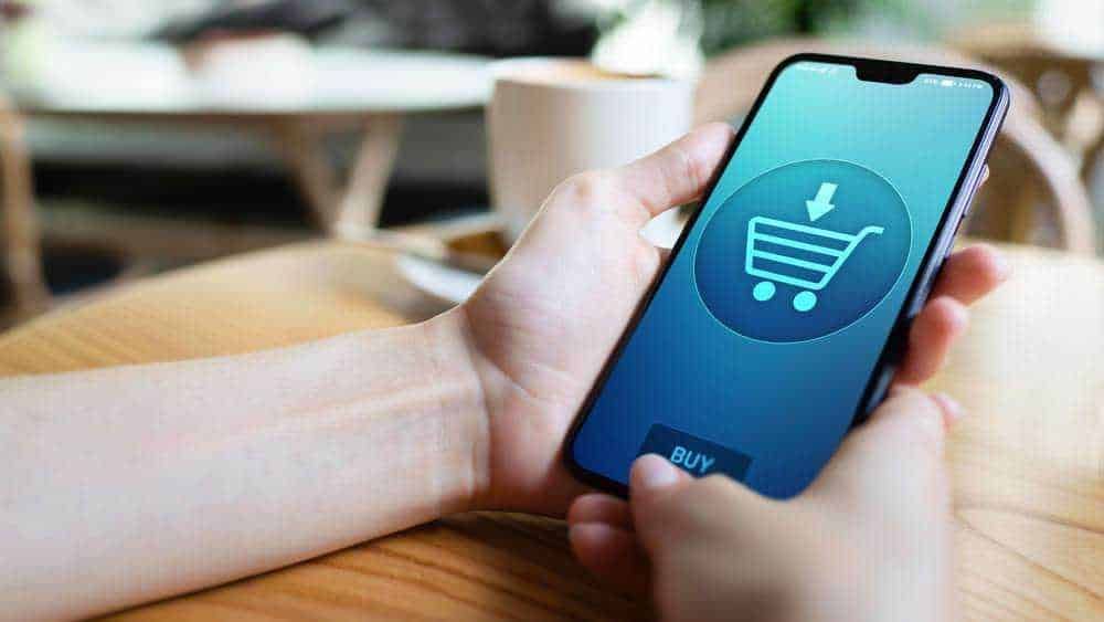 Acquisto online tramite smartphone con icona carrello della spesa digitale.