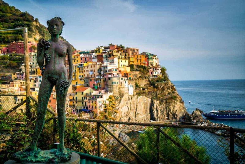 Domenica delle Palme 2023: Esperienza unica nel Nord Italia 3 Femminile statua in bronzo sul promontorio di Manarola con visione del borgo colorato delle Cinque Terre e il Mar Ligure sullo sfondo, Italia.