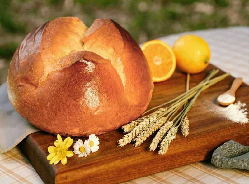 Domenica delle Palme 2023: Esperienza unica nel Nord Italia 5 Pane casereccio rustico con scorza dorata, accompagnato da arancia fresca e spiga di grano su tagliere di legno, ideale per ricette tradizionali italiane.