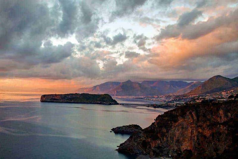 Scegliere un villaggio turistico in Calabria, tra Vibo Valentia 2 Villaggi turistici in calabria: Scorcio panoramico del mare al tramonto con montagne sullo sfondo e cielo nuvoloso, vista naturale di alta qualità.