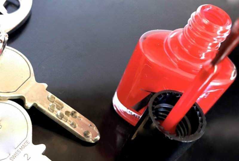 Vernice rossa per auto o moto, con pennello e tappo aperto, su superficie scura.