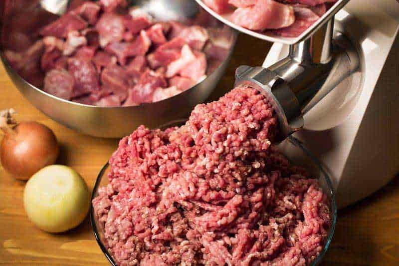 Macinato di carne fresca con affettatrice e cipolle sul piano di lavoro in cucina.
