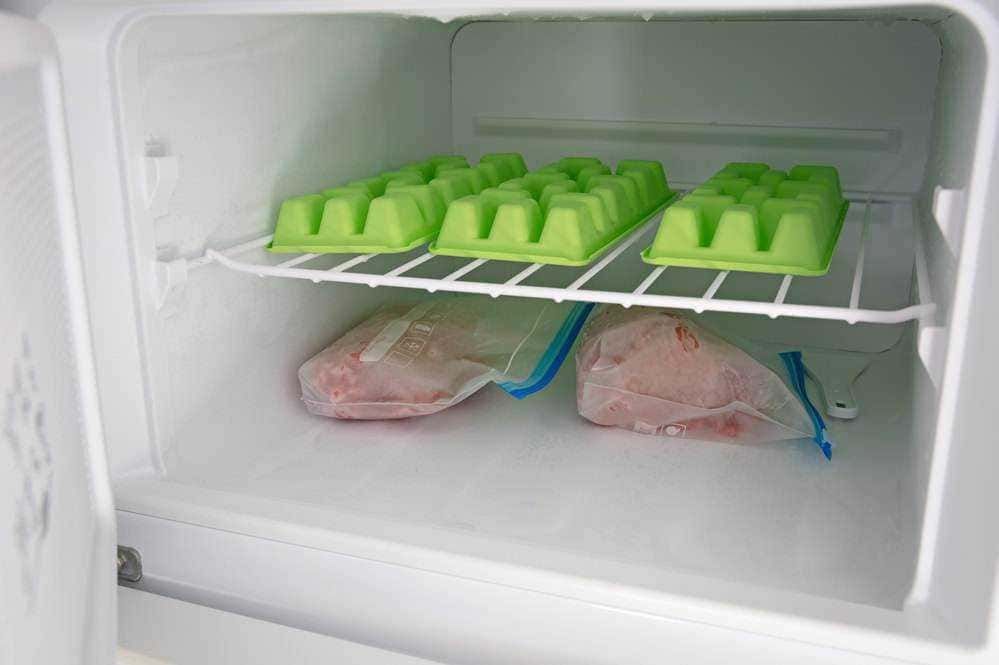 Palline di ghiaccio nel freezer, cubetti di ghiaccio in vaschetta di plastica congelati, freezer vuoto con sacchetti di ghiaccio, preparazione ghiaccio in casa, conservazione alimenti congelati, ghiaccio fai da te per bevande fredde.