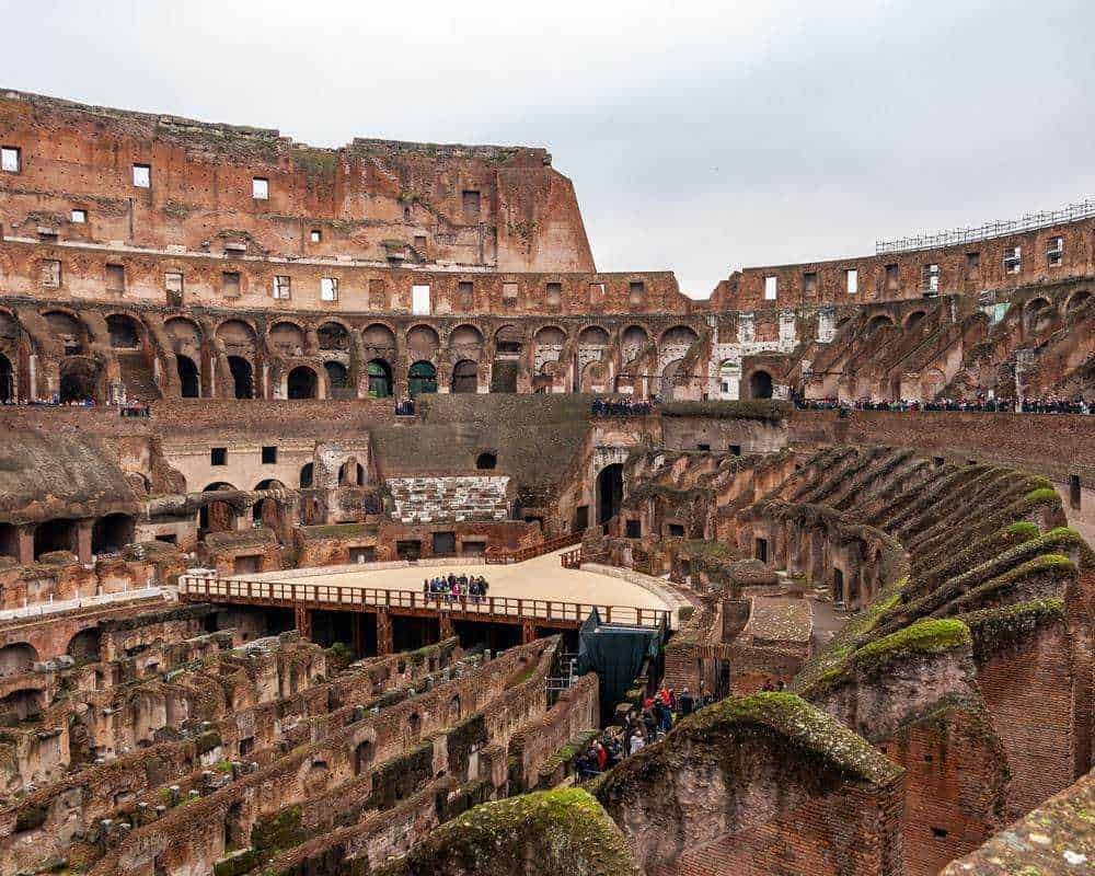 Ruins del Colosseo, antica arena romana, con molte strutture sotterranee visibili, pubblico e guide turistiche, cielo nuvoloso, struttura archeologica Patrimonio dell'umanità UNESCO, attrazione turistica Roma.
